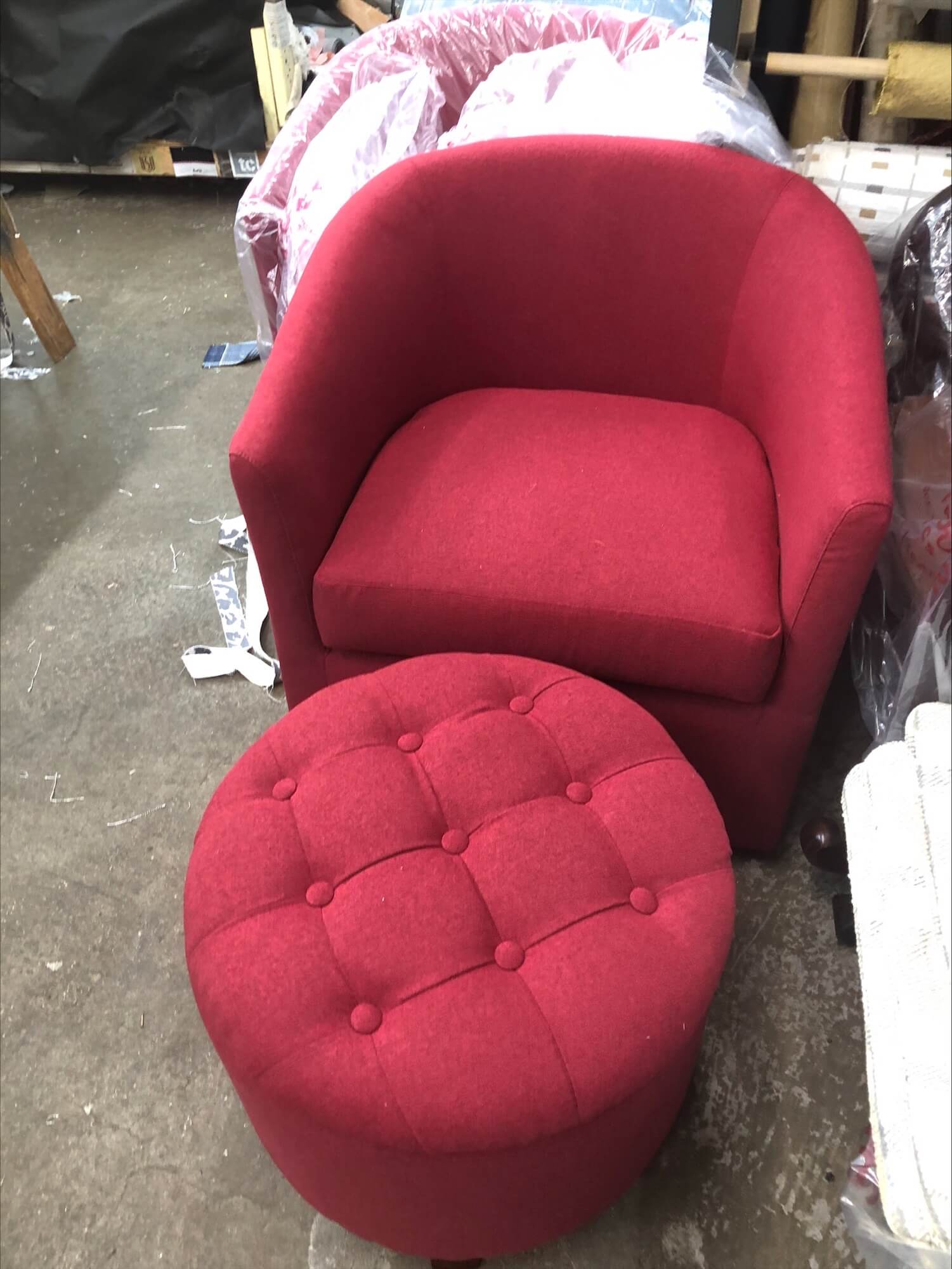 Red upholstered armchair paired with a matching tufted ottoman, set against a cluttered background. Ideal for cozy living spaces.